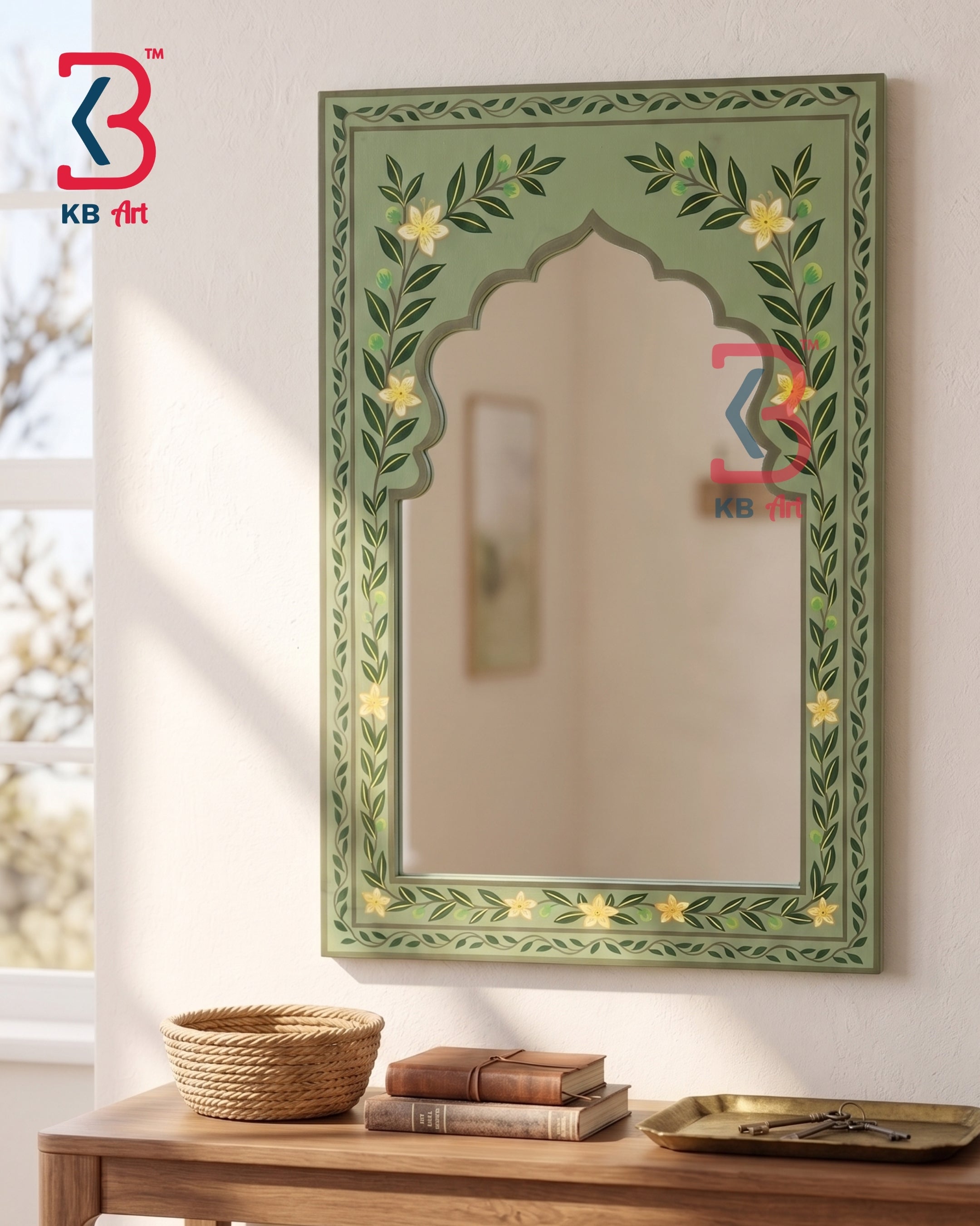 An ornate arched wall mirror with a sage green frame decorated with hand-painted yellow flowers and green leaves, mounted on a white wall above a wooden console table with books and a woven basket.