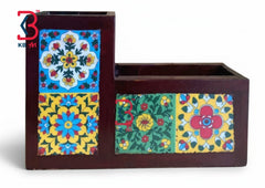 A dark brown wooden desk organizer with two compartments, decorated with colorful hand-painted floral and geometric tile patterns on the front panels, shown against a plain white background.