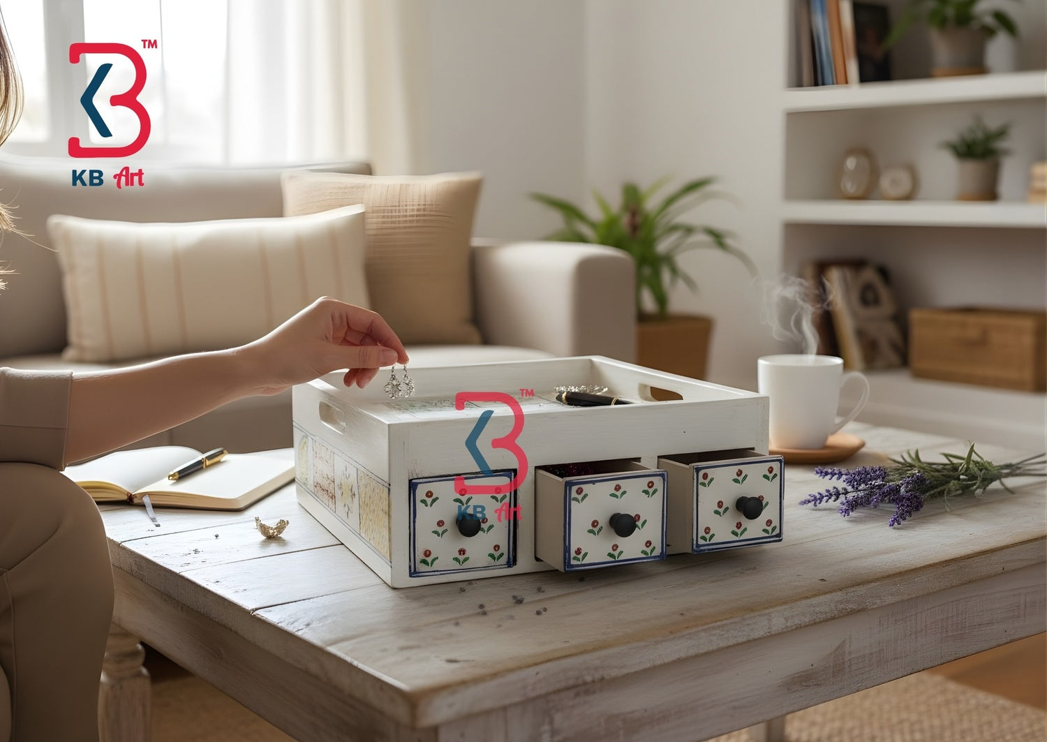 A white decorative storage box with three drawers and floral detailing sits on a wooden coffee table in a cozy living room setting. A person's hand is reaching into the top compartment, and a white mug, lavender sprigs, and an open notebook are nearby. An AI-edited lifestyle scene displaying the wooden 3-drawer tray neatly styled with teacups on a cozy living room coffee table.