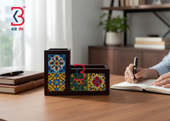A dark brown wooden desk organizer with colorful geometric tile patterns on its front panels, shown on a wooden desk next to a person writing in a notebook.