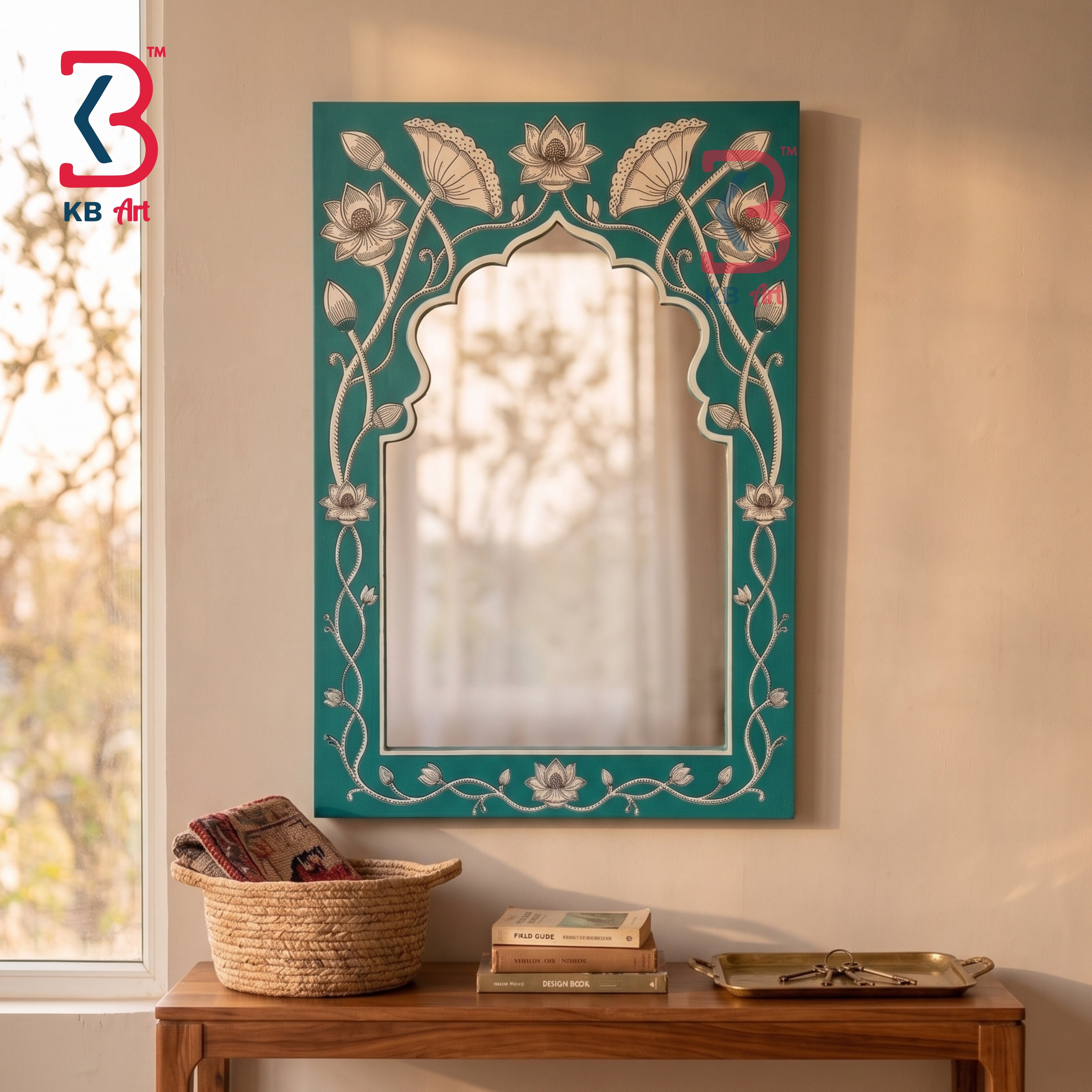 A decorative arched wall mirror with a teal green frame featuring white floral and vine motifs, hanging on a beige wall above a wooden console table with a basket and books.