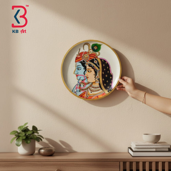 Round wooden wall plate with hand-painted Radha Krishna side-profile portrait, peacock feather crown, gold rim, on ivory background