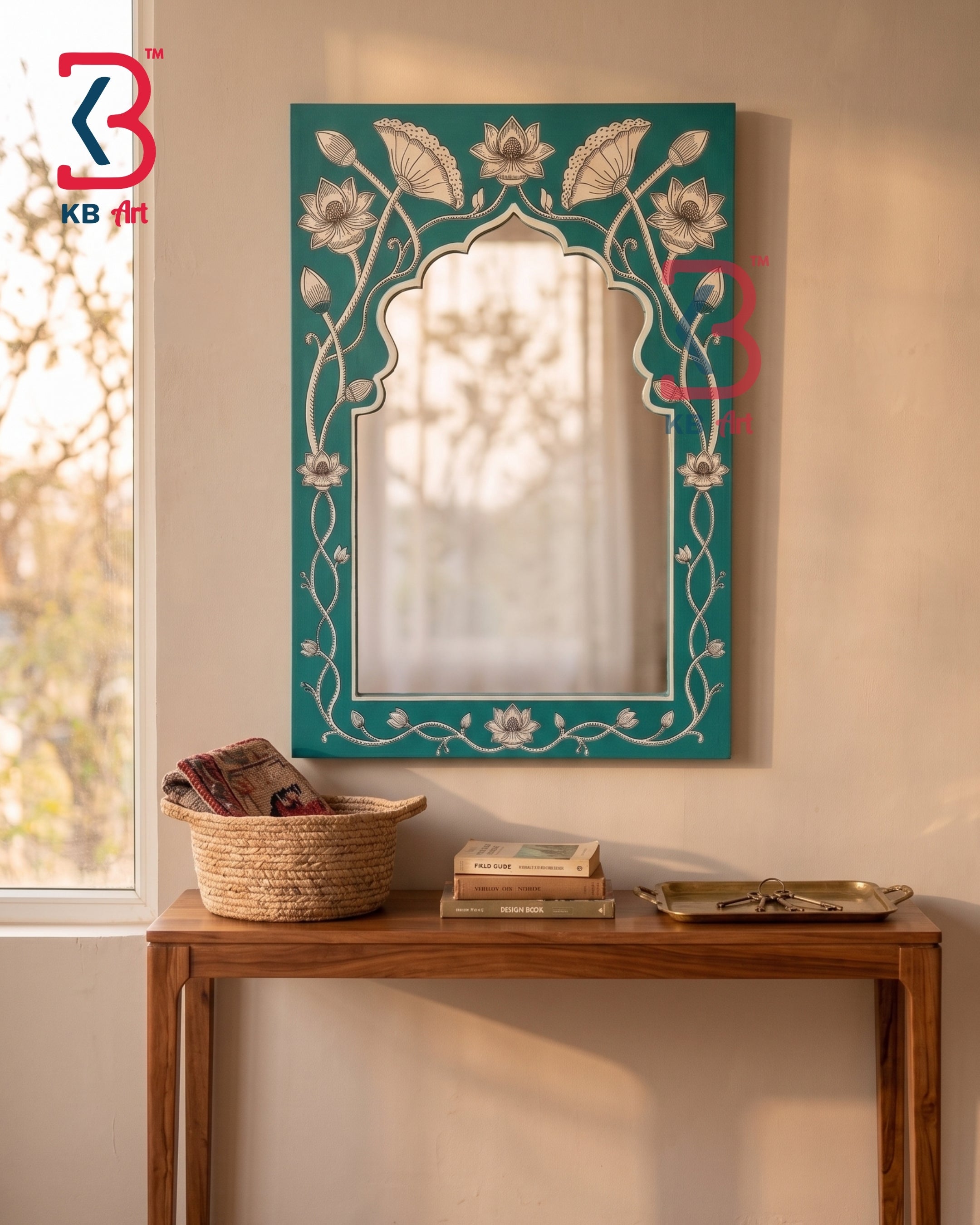 A decorative rectangular wall mirror with an arched center and ornate floral border, mounted above a wooden console table in a warm beige room. The frame is teal with white floral and vine motifs.