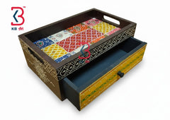 A decorative wooden storage box with a tray top and one pulled-out drawer, shown on a plain white background. The box has multicolored patterned inlay panels on the tray and drawer front, dark brown sides, and a yellow-gold drawer pull area.