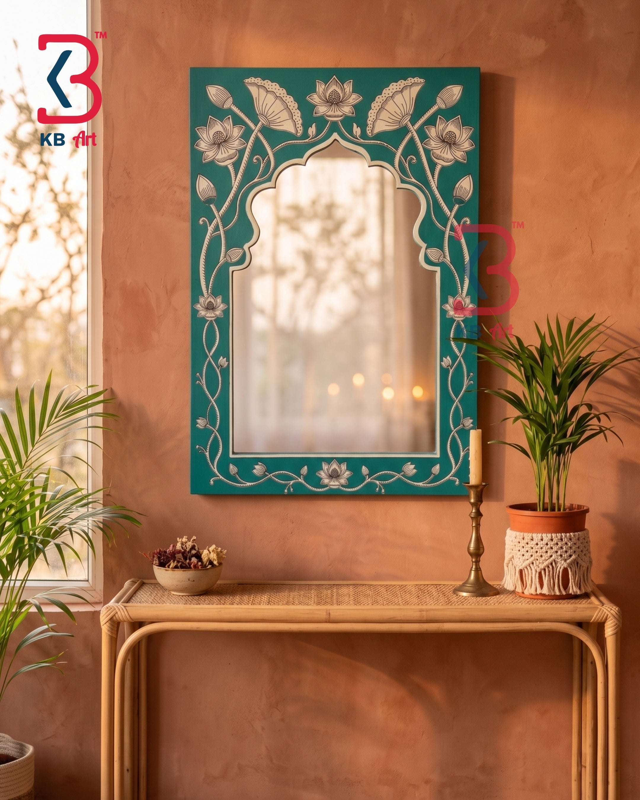 A decorative teal wall mirror with intricate white floral and vine patterns, mounted on a terracotta-colored plaster wall above a bamboo console table with plants.