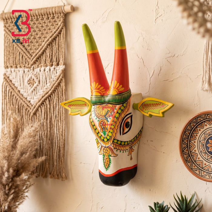 Multicolor hand-painted wooden cow head wall hanging with orange horns, yellow sunburst and floral pendant design on white background
