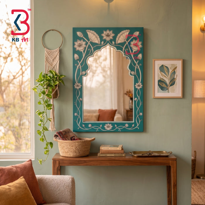 A decorative arched wall mirror with a teal blue frame and white floral vine patterns, mounted on a sage green wall above a wooden console table in a styled living room setting.