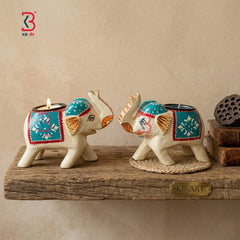 KB ART pair of ethnic hand-painted wooden elephant tea-light candle holders with teal and red blankets on an antique white-wood body against a white background.